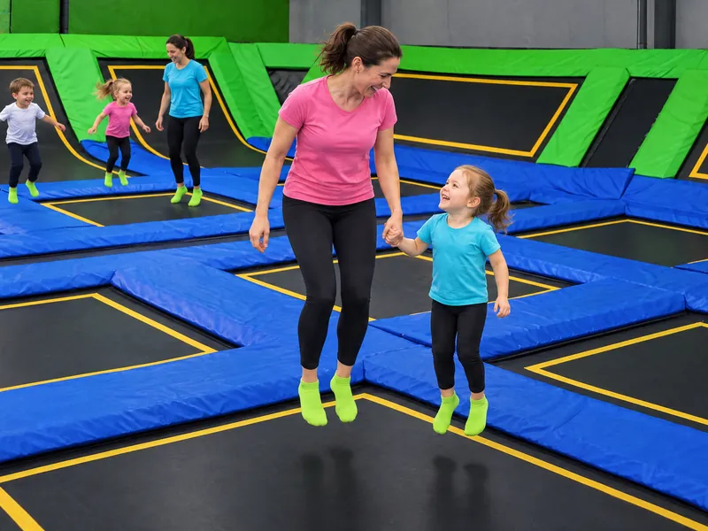 Opiekunka trzyma przedszkolaka za rękę i razem skaczą na trampolinie (obraz wygenerowany przez AI)