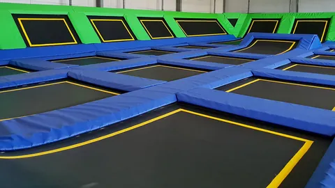 Pola trampolin z żółtymi ramkami i zielone ściany odbiciowe w Jumpout