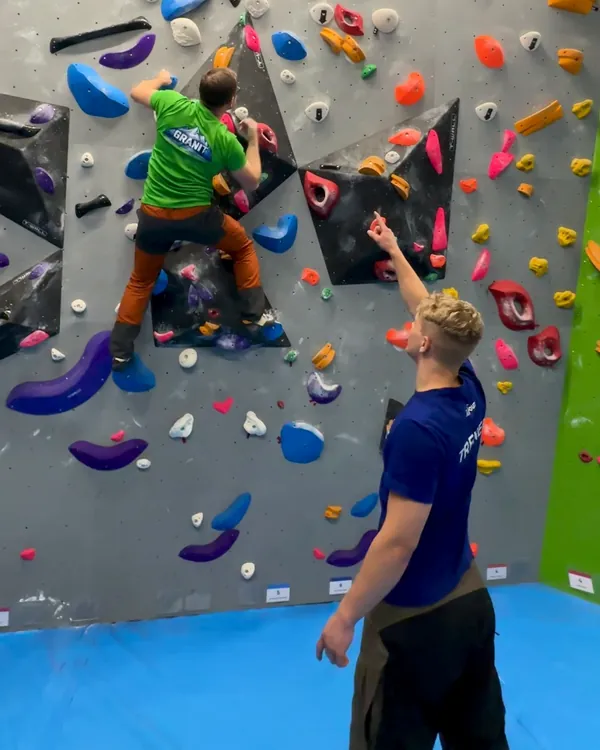 Trener wskazuje chwyt wspinaczowi na ściance boulderowej w Jumpout