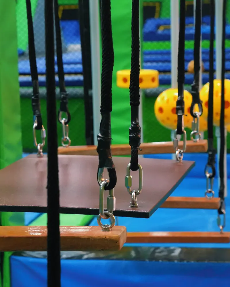 Huśtawki toru ninja na łańcuchach w Jumpout, w tle żółte kule, niebieskie maty i limonkowe ściany