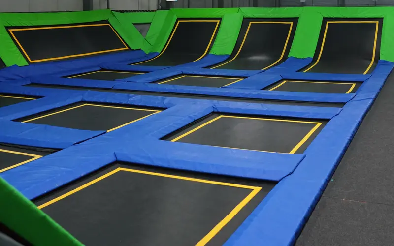 Czarne pola trampolin z żółtym obrysem i kobaltowe maty w hali Jumpout