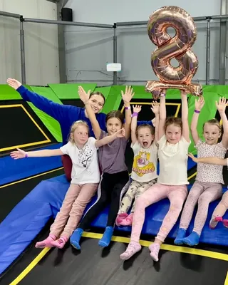 Animatorka w granatowej bluzie z dziewczynkami z urodzin, ręce w górze, nad nimi balon w kształcie ósemki