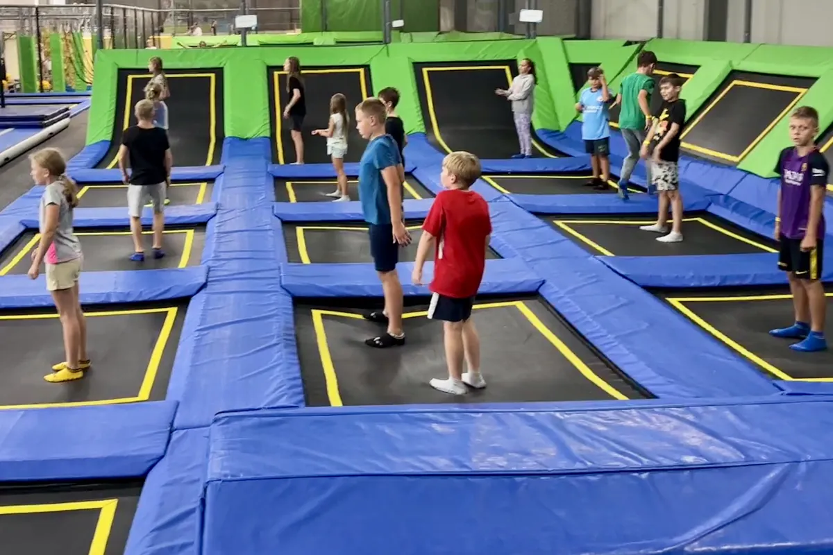 Dzieci na polach trampolin w hali Jumpout, w głębi kolejne pola i zielone ściany