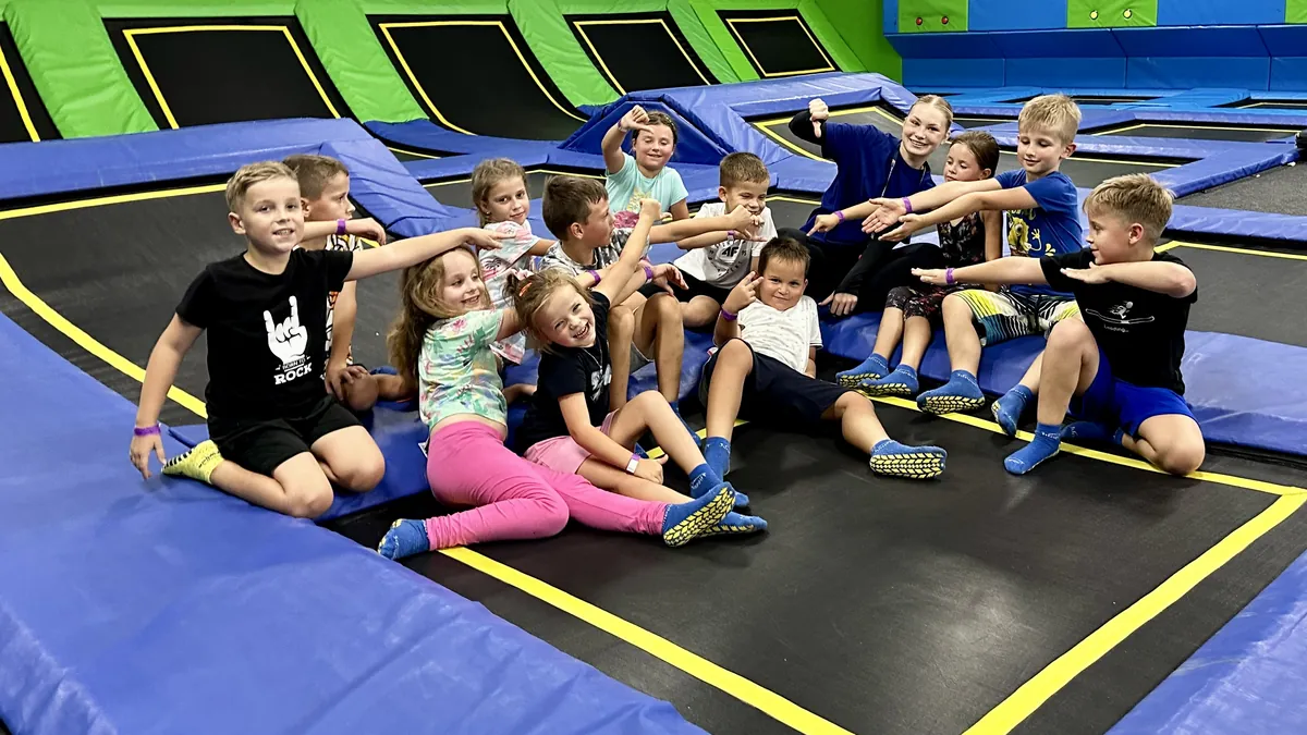 Animatorka w granatowej bluzie siedzi z grupą urodzinową na trampolinie, dzieci wskazują na nią
