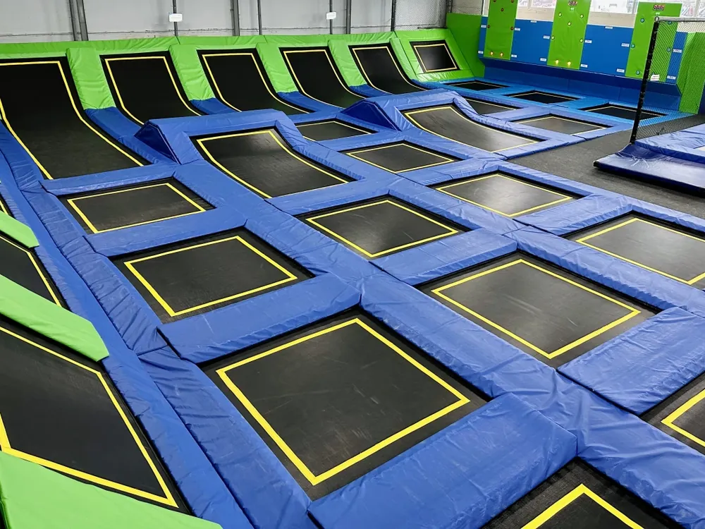 Główna arena trampolin Jumpout: czarne pola z żółtym obrysem, niebieskie obicia i skośne trampoliny przy ścianach